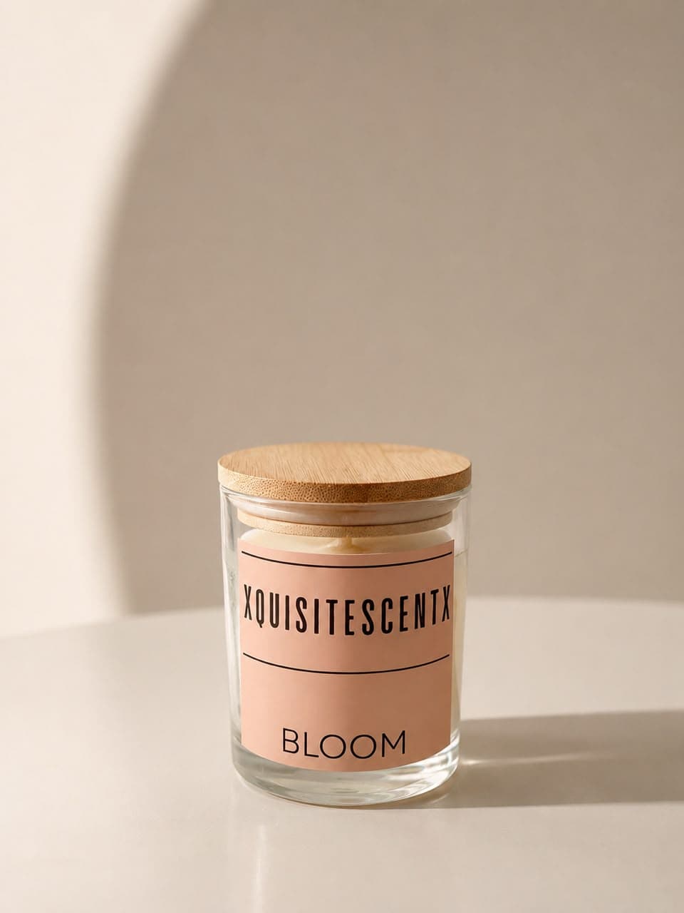 A Bloom soy candle in clear glass with a bamboo lid, its blush XQUISITESCENTX label facing the camera